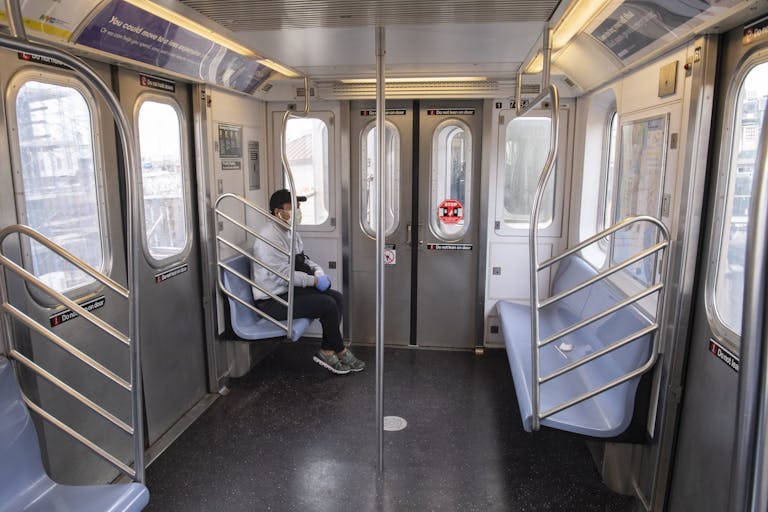 A man wearing a mask and gloves rides an empty subway train car
