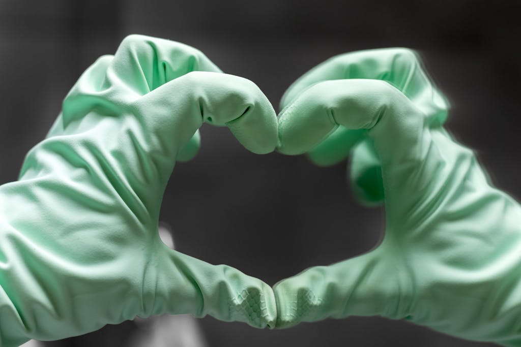 A hand in a mint green rubber glove shows a heart sign.