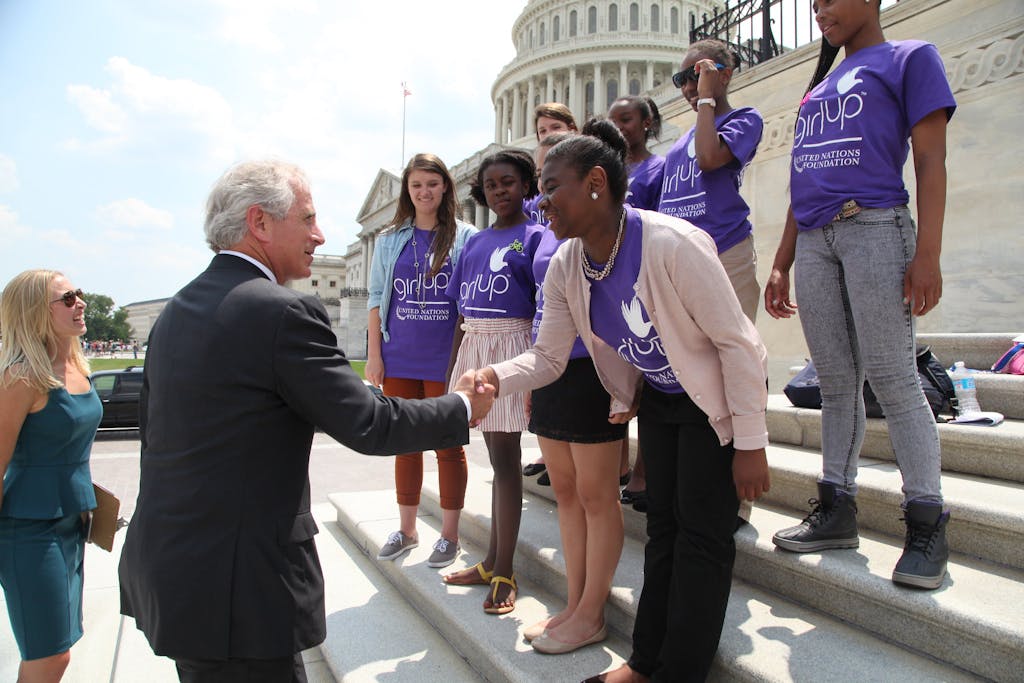 A Black girl shakes hands with man wearing a suit on the steps of the Capitol